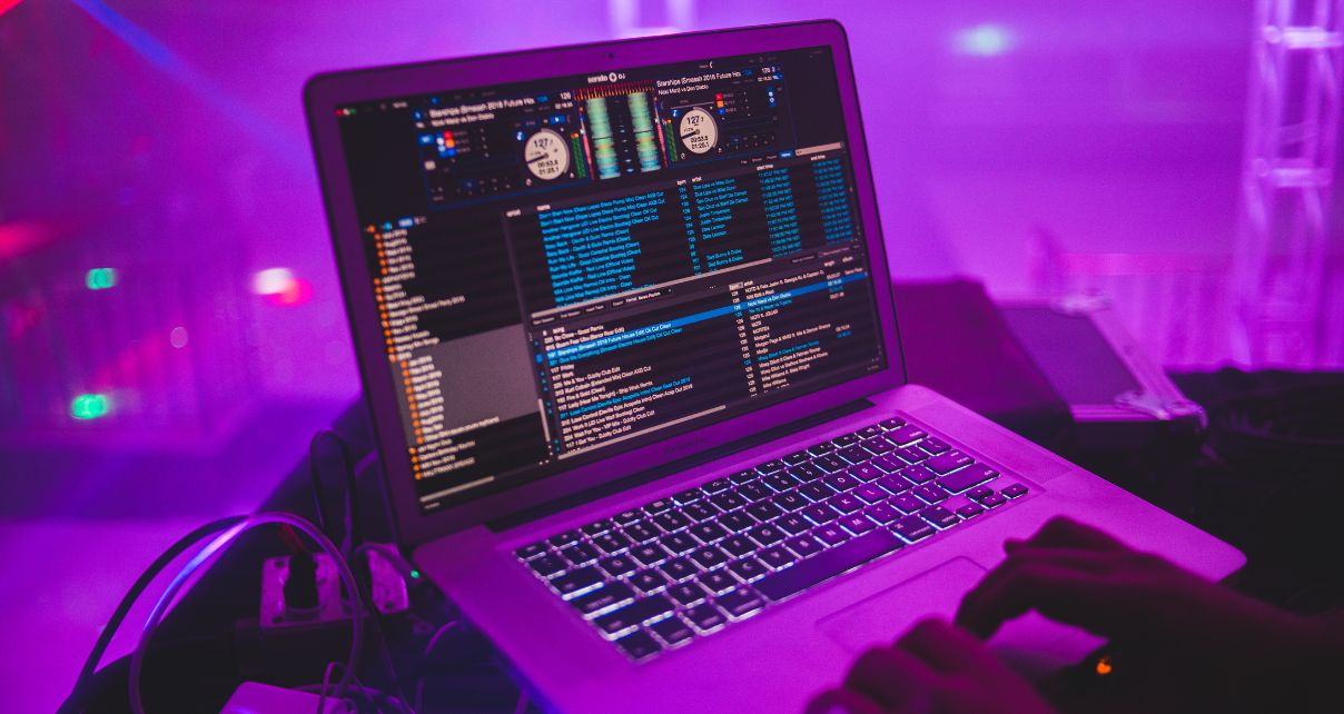 DJ using a laptop looking through their laptop music in a mostly empty club, purple lighting