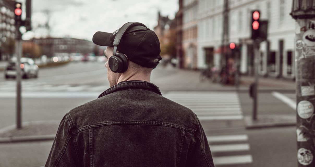 Man in a hat and headphones standing at a street corner listening to music