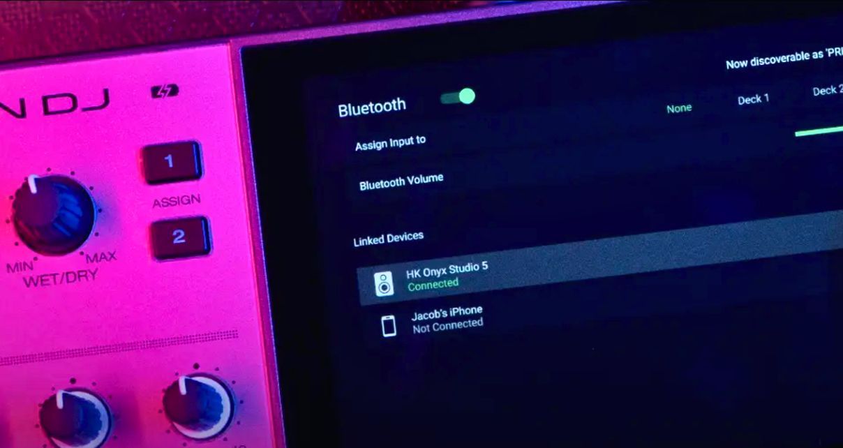 Moody zoomed in picture of the screen on a Denon DJ Prime Go+ DJ system showing Bluetooth out bathed in pink lighting